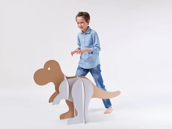 Pequeño niño soñador jugando con un dinosaurio de cartón Tyrannosaurus rex. Infancia. Fantasía, imaginación . — Foto de Stock