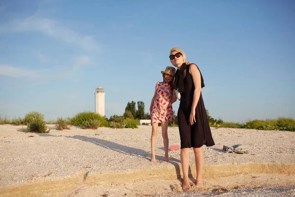 Leende mor och vacker dotter har roligt på stranden. Porträtt av lycklig kvinna ger en piggyback rida till söt liten flicka med kopieringsutrymme. Porträtt av barn som omfamnar sin mamma under sommaren. — Stockfoto