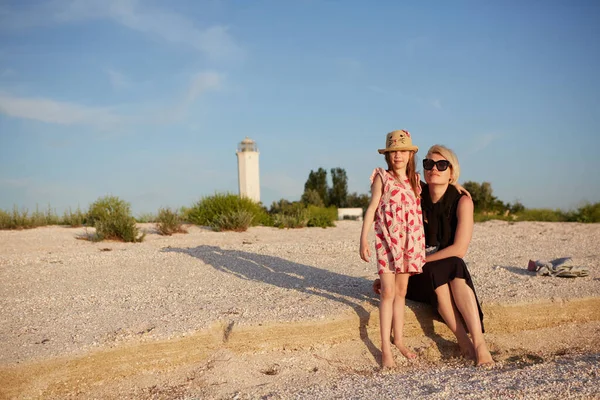 Madre sorridente e bellissima figlia si divertono sulla spiaggia. Ritratto di donna felice che dà un passaggio a cavalluccio a simpatica bambina con spazio copia. Ritratto di bambina che abbraccia sua madre durante l'estate. — Foto Stock