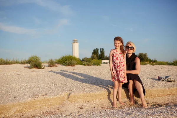 Madre sorridente e bellissima figlia si divertono sulla spiaggia. Ritratto di donna felice che dà un passaggio a cavalluccio a simpatica bambina con spazio copia. Ritratto di bambina che abbraccia sua madre durante l'estate. — Foto Stock