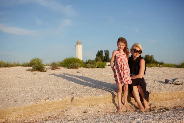 Uśmiechnięta matka i piękna córka bawią się na plaży. Portret szczęśliwej kobiety dającej przejażdżkę na barana słodkiej dziewczynce z przestrzenią do kopiowania. Portret dziecka obejmującego jej mamę latem. — Zdjęcie stockowe