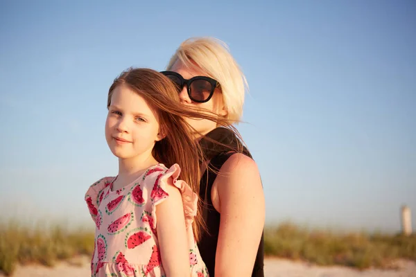 笑顔の母親と美しい娘がビーチで楽しんでいます。コピースペース付きの可愛い女の子にピギーバックライドを与える幸せな女性の肖像画。夏の間に母親を抱きしめる子供の肖像. — ストック写真