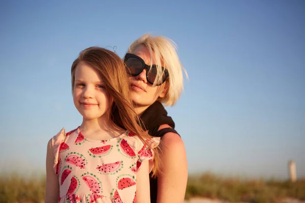 Usmívající se matka a krásná dcera se baví na pláži. Portrét šťastné ženy dává svezení prasátko roztomilé holčičce s kopírovacím prostorem. Portrét dítěte objímající svou matku v létě. — Stock fotografie