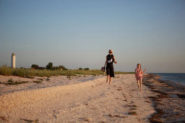 Smiling mother and beautiful daughter having fun on the beach. Portrait of happy woman giving a piggyback ride to cute little girl with copy space. Portrait of kid and her mom during summer — Stock Photo, Image