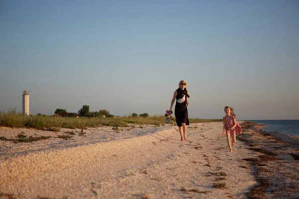 Smiling mother and beautiful daughter having fun on the beach. Portrait of happy woman giving a piggyback ride to cute little girl with copy space. Portrait of kid and her mom during summer — Stock Photo, Image