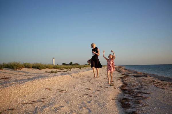 笑顔の母親と美しい娘がビーチで楽しんでいます。コピースペース付きの可愛い女の子にピギーバックライドを与える幸せな女性の肖像画。夏の間の子供と彼女の母親の肖像 — ストック写真