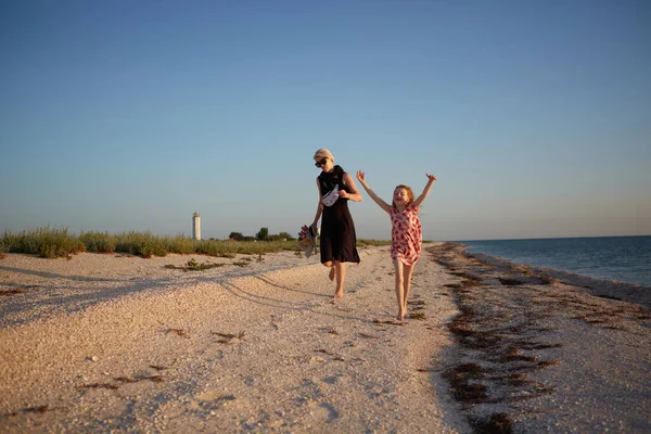 Lachende moeder en mooie dochter die plezier hebben op het strand. Portret van een gelukkige vrouw die een ritje op haar rug geeft aan een schattig klein meisje met kopieerruimte. Portret van kind en haar moeder tijdens de zomer — Stockfoto