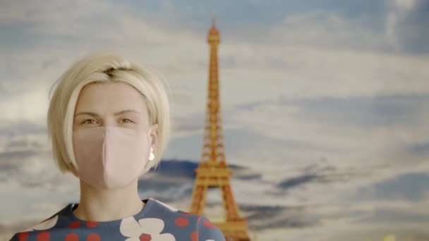 Portret van een mooie blonde jonge vrouw die een beschermend medisch masker draagt en voor de Eiffeltoren staat. Veilige en gelukkige vrouw oefenen van sociale afstand. — Stockvideo