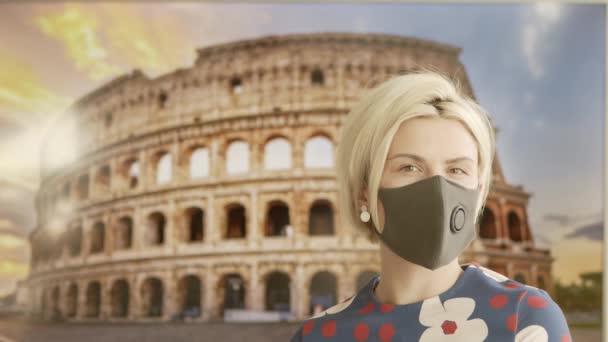 Ritratto di una bella giovane donna bionda che indossa una maschera protettiva medica e si trova di fronte al Colosseo. Donna sicura e felice che pratica la distanza sociale. Concetto di viaggio online. — Video Stock