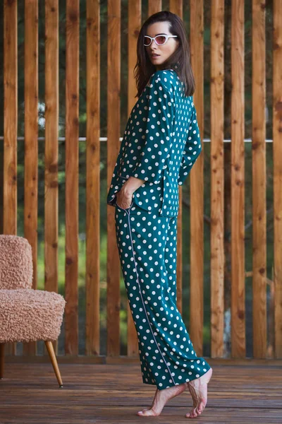 Woman standing in pajamas pajamas with polka dots on wooden background in full length. Caucasian female model.