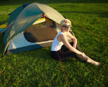 Seyahat, kano ve yürüyüş konsepti. Genç ve güzel bir kadının portresi yeşil çadırın yanında oturuyor ve nehir kenarında kano var..