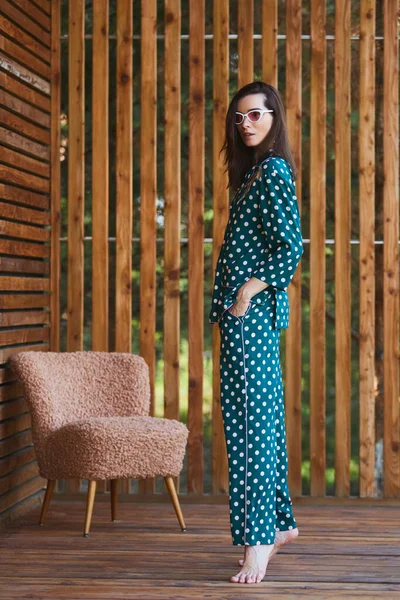 Woman standing in pajamas pajamas with polka dots on wooden background in full length. Caucasian female model.
