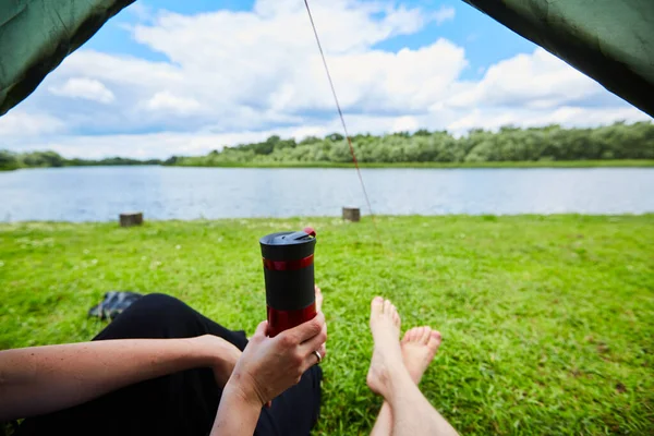 Twee paar benen steken uit de tent op een grasveld en in de buurt van de rivier. — Stockfoto