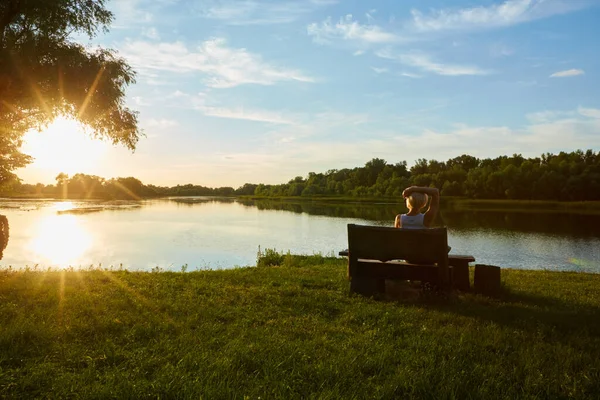 Mulher sentada no banco durante um belo pôr do sol — Fotografia de Stock