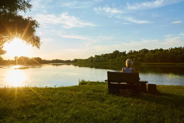 Kobieta siedzi na ławce podczas pięknego zachodu słońca — Zdjęcie stockowe
