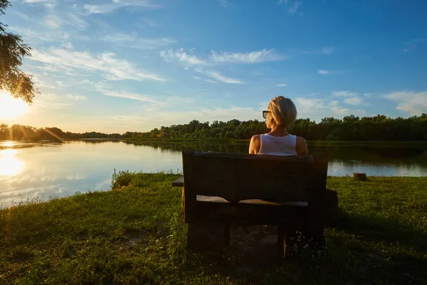 Kobieta siedzi na ławce podczas pięknego zachodu słońca — Zdjęcie stockowe
