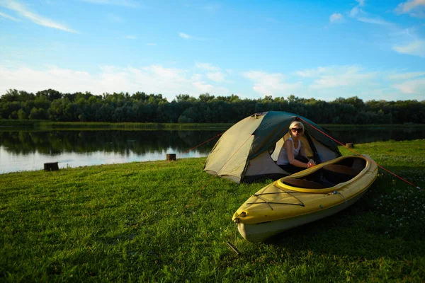 Cestování, jízda na kajaku a turistika. Portrét mladé krásné ženy sedící v blízkosti zeleného stanu s kajakem v blízkosti řeky. — Stock fotografie