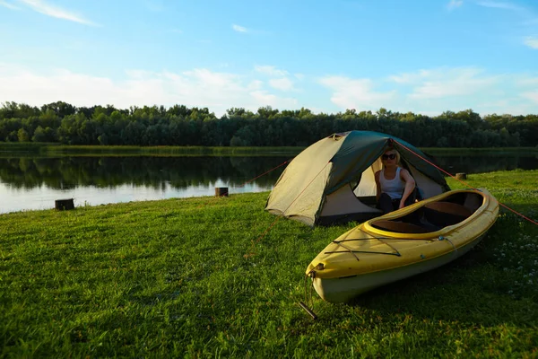 Cestování, jízda na kajaku a turistika. Portrét mladé krásné ženy sedící v blízkosti zeleného stanu s kajakem v blízkosti řeky. — Stock fotografie