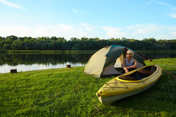 Reizen, kajakken en wandelen concept. Portret van een mooie jonge vrouw in de buurt van een groene tent met kajak bij de rivier. — Stockfoto