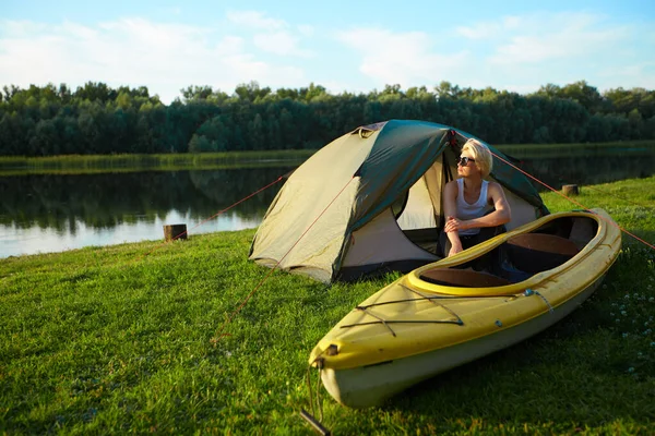 Concept de voyage, kayak et randonnée. Portrait de jeune belle femme assise près d'une tente verte avec kayak près de la rivière. — Photo