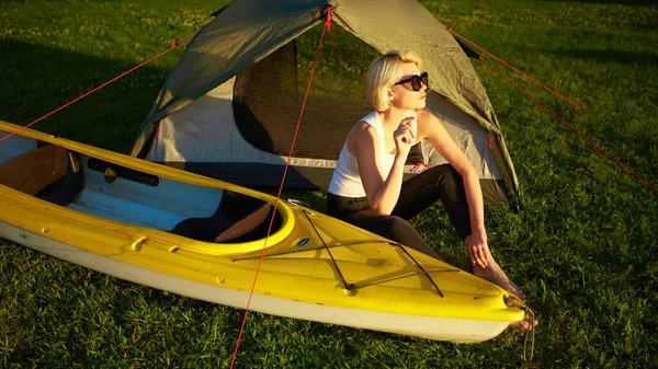 Resor, kajakpaddling och vandring koncept. Porträtt av ung vacker kvinna sitter nära grönt tält med kajak nära floden. — Stockfoto