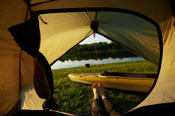 Pies de mujeres jóvenes relajándose con vista al lago desde la entrada de la tienda de campaña al aire libre. Travel wanderlust estilo de vida concepto aventura vacaciones al aire libre, vacaciones de verano y viaje de vacaciones —  Fotos de Stock