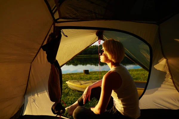 Ung kvinna resenär sitter i tältet, avkopplande och med vacker soluppgång — Stockfoto