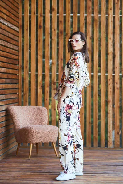 Mulher sexy elegante jovem em pijama em pé no terraço em hotel tropical, palmeiras fundo, cabelo preto longo, óculos de sol, brincos, óculos de sol . — Fotografia de Stock