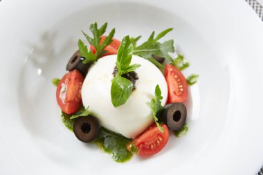İtalyan domateslerinin üzerine beyaz yuvarlak top şeklinde İtalyan burrata peyniri konmuş geleneksel otantik yumuşak ve kremalı İtalyan burrata peyniri.