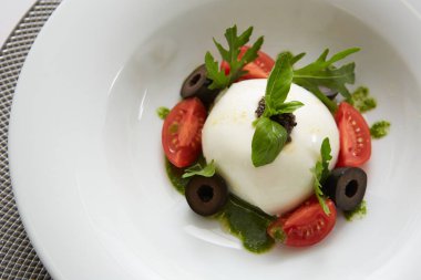 İtalyan domateslerinin üzerine beyaz yuvarlak top şeklinde İtalyan burrata peyniri konmuş geleneksel otantik yumuşak ve kremalı İtalyan burrata peyniri.
