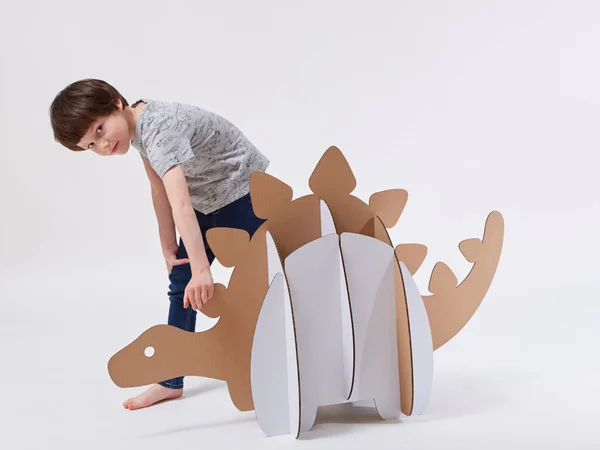 Pequeño niño soñador jugando con un dinosaurio de cartón Stegosaurus. Infancia. Fantasía, imaginación —  Fotos de Stock