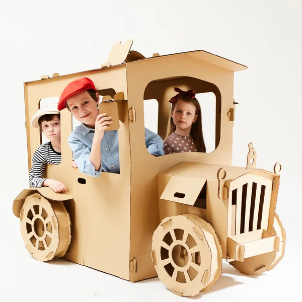 Creative children plays in cardboard car playhouse.