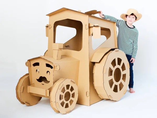 Un niño está jugando con un tractor de cartón sobre un fondo blanco. Concepto agrícola. Mockup para el diseño con espacio de copia. —  Fotos de Stock