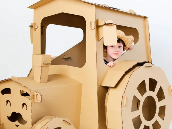 Un niño está jugando con un tractor de cartón sobre un fondo blanco. Concepto agrícola. Mockup para el diseño con espacio de copia. —  Fotos de Stock