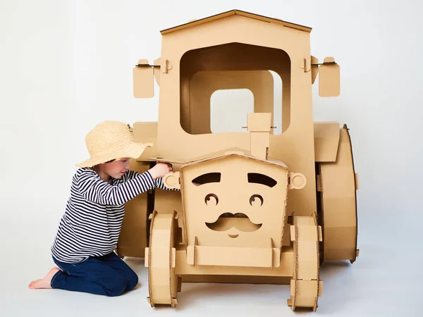 A little boy is playing with cardboard tractor on a white background. Agriculture concept. Mockup for design with copy space. — Stock Photo, Image