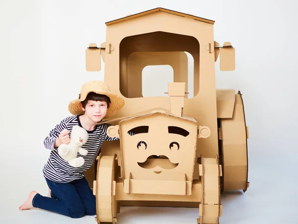 Un niño está jugando con un tractor de cartón sobre un fondo blanco. Concepto agrícola. Mockup para el diseño con espacio de copia. — Foto de Stock