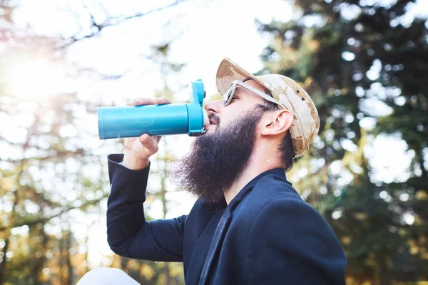 Ritratto di bell'uomo barbuto che beve tè caldo all'aperto in viaggio a piedi. L'uomo forte e coraggioso con barba ha un riposo su sentiero escursionistico. Tempo di relax. — Foto Stock