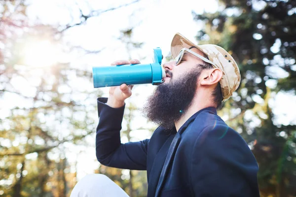 Bearded man drinking coffee in the woods after work — Stock Photo, Image