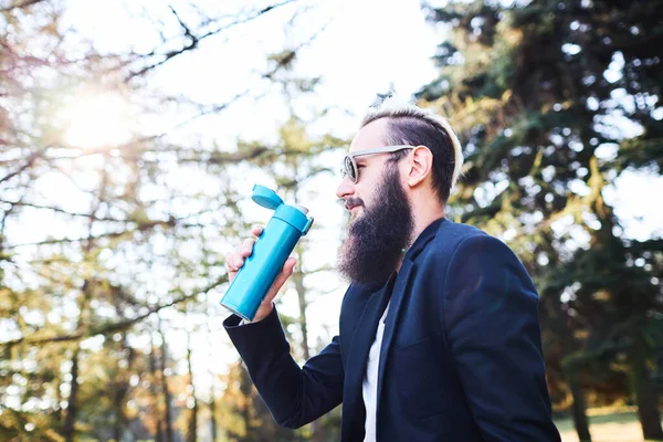 Portrait of handsome bearded man drinking hot tea outdoor in trip on foot. Strong and brave man with beard have a rest on hiking trail. Time for relax. — Stock Photo, Image