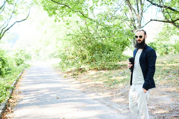 Porträt eines gutaussehenden bärtigen Mannes, der im Freien zu Fuß heißen Tee trinkt. Kräftige und tapfere Männer mit Bart ruhen sich auf Wanderwegen aus. Zeit zum Entspannen. — Stockfoto