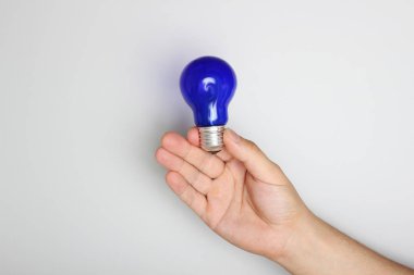 hafif bir arka plan üzerinde elinde mavi ampul