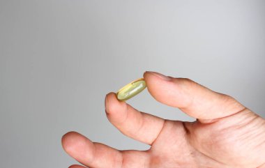 hafif bir arka plan üzerinde elinde sarı kapsül