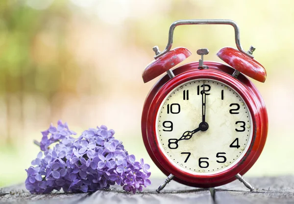 Reloj despertador rojo y flor púrpura, horario de verano, primavera — Foto de Stock