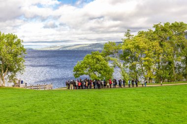 A scenic view of Loch Ness and highlands with a group of tourists standing and waiting for a return boat, Scotland clipart