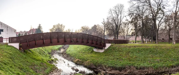 Uma ponte de madeira cênica sobre um pequeno riacho perto do Castelo de Zrinyi no início da manhã, Szigetvar, Hungria — Fotografia de Stock