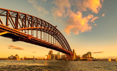 Altın gün batımında Sydney Harbour Köprüsü ve Opera Binası