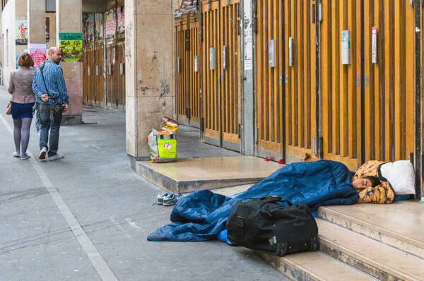 People pass by a young sleeping man on the street in Paris. The problem of refugees and migrants in Europe. Paris, France, October 04, 2014.