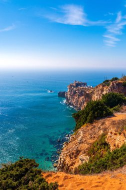 Portekiz 'in deniz kıyısındaki antik kale, Nazare. Kayalık kayalıklardaki deniz feneri. Atlantik Okyanusu kıyısı. Promontuarın yamaçları yeşil bitkilerle kaplıdır. Dalgalar kayalara çarpıyor..