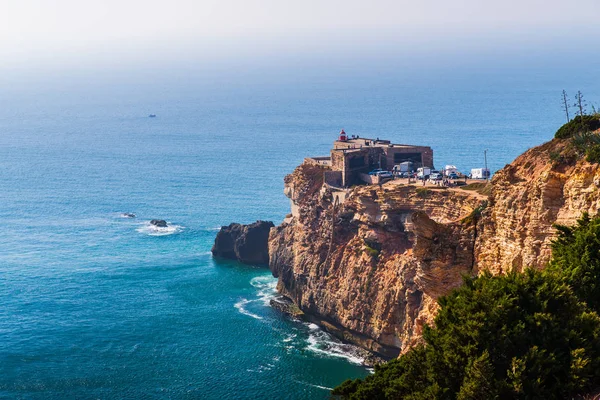 Portekiz 'in deniz kıyısındaki antik kale, Nazare. Kayalık kayalıklardaki deniz feneri. Atlantik Okyanusu kıyısı. Promontuarın yamaçları yeşil bitkilerle kaplıdır. Dalgalar kayalara çarpıyor..