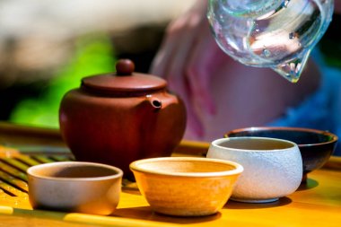 Tahta tepside masada çaylı çaydanlık, çaydanlık, bardak. Adam, eller çay döküyor.
